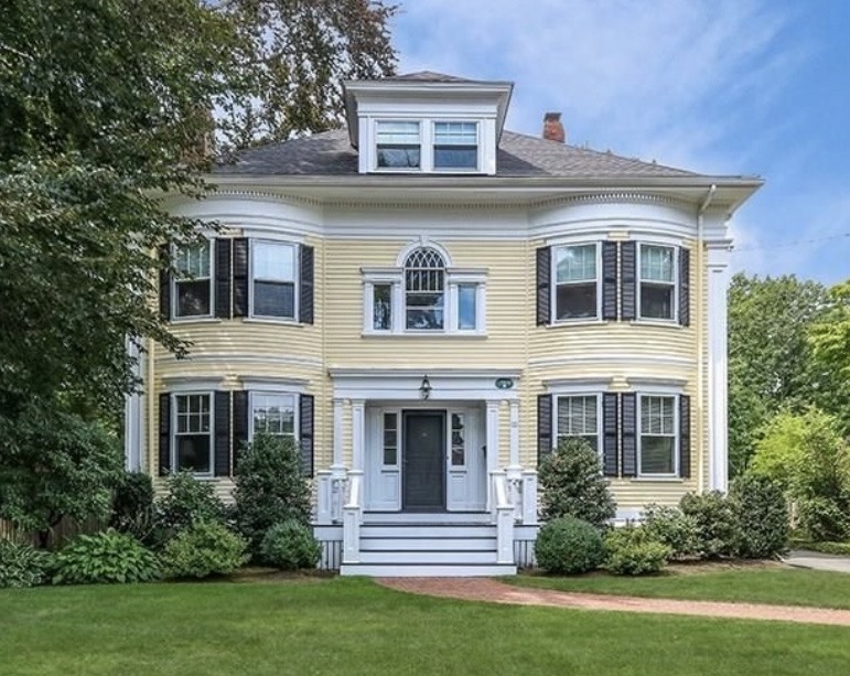 Hawkes Home Services home base: a pale yellow two-story Colonial in Dedham, Massachusetts with white trim, black shutters, curved bay windows and a columned front portico